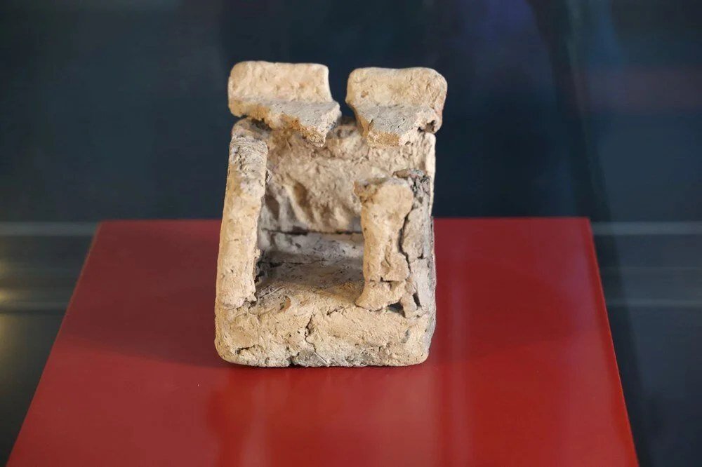 A small Neolithic architectural model — a little clay-and-stone structure with uprights framing an interior