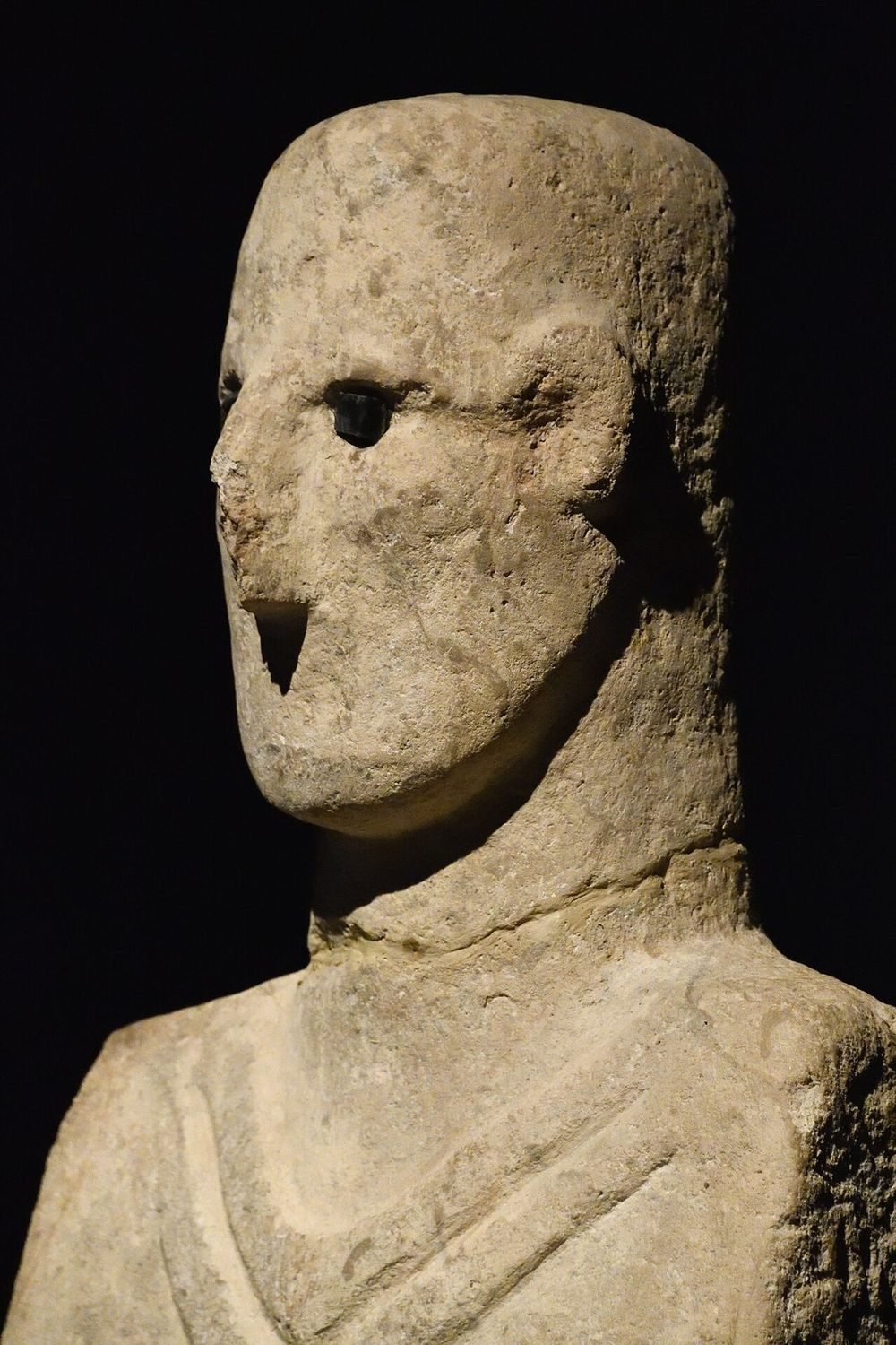 Seen from the side, one obsidian eye still holds its socket and the nose reads as a sharp ridge broken at the tip. The back of the head is left plain and rounded — the sculptor concentrated the detail on the face and chest.