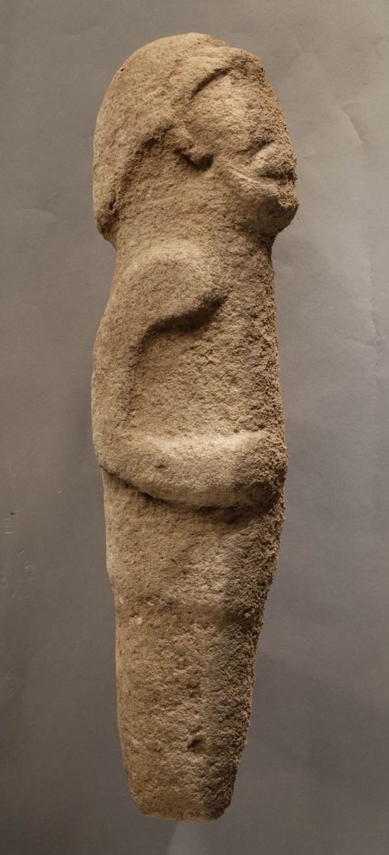 The complete limestone figure — arms folded to the belly — found lying face-down beside a pillar.