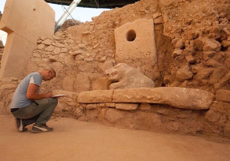 A researcher crouches beside the life-size stone boar on the carved bench, documenting it