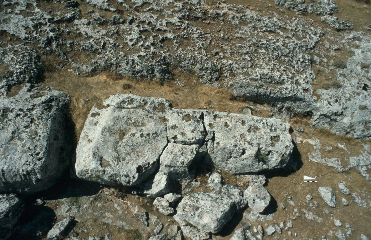 An unfinished T-pillar, around seven metres long, still attached to the bedrock where it was being cut — the work abandoned mid-task.