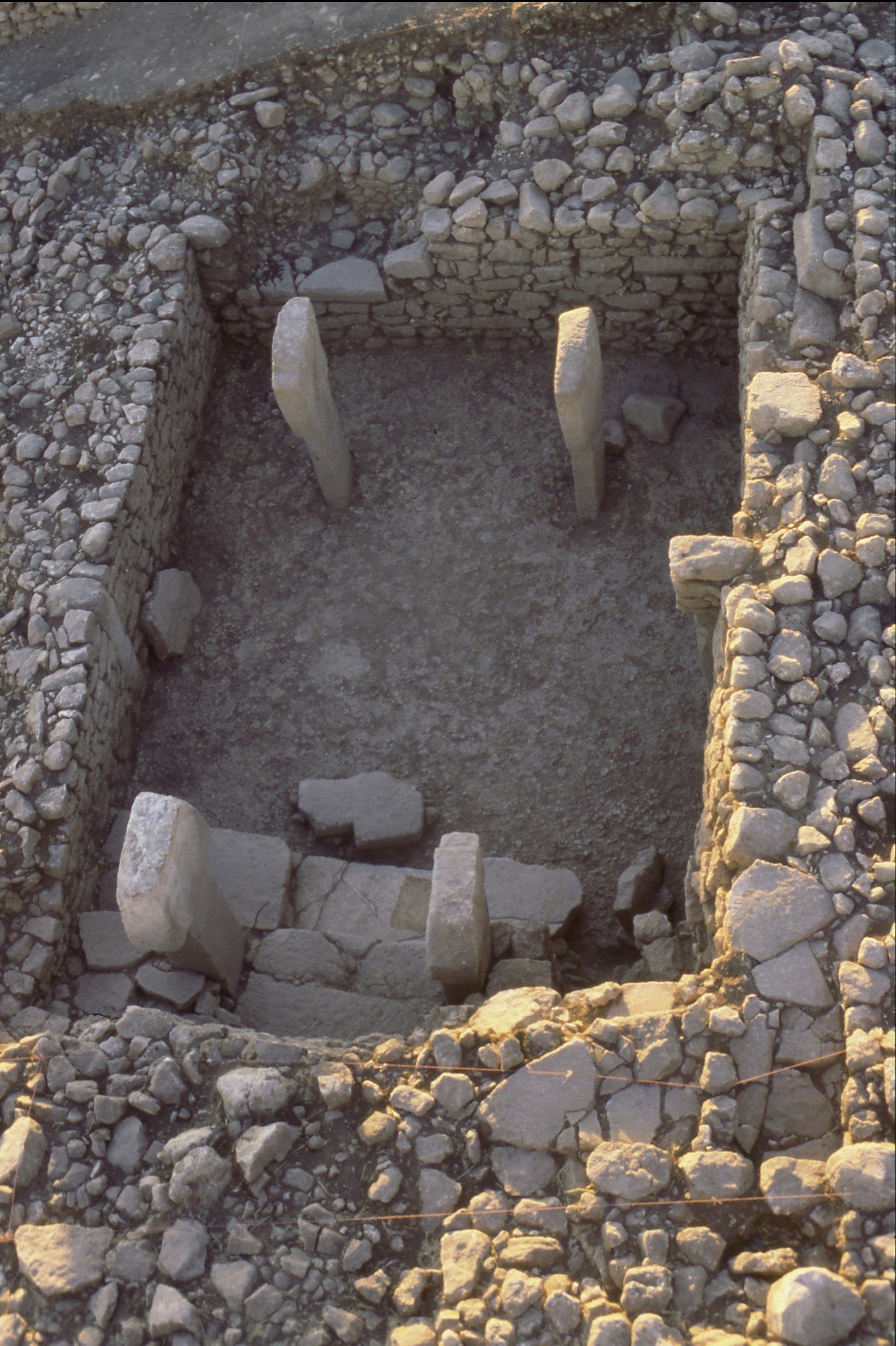 Overhead view of a rectangular room with two standing T-pillars at the back and toppled blocks in front