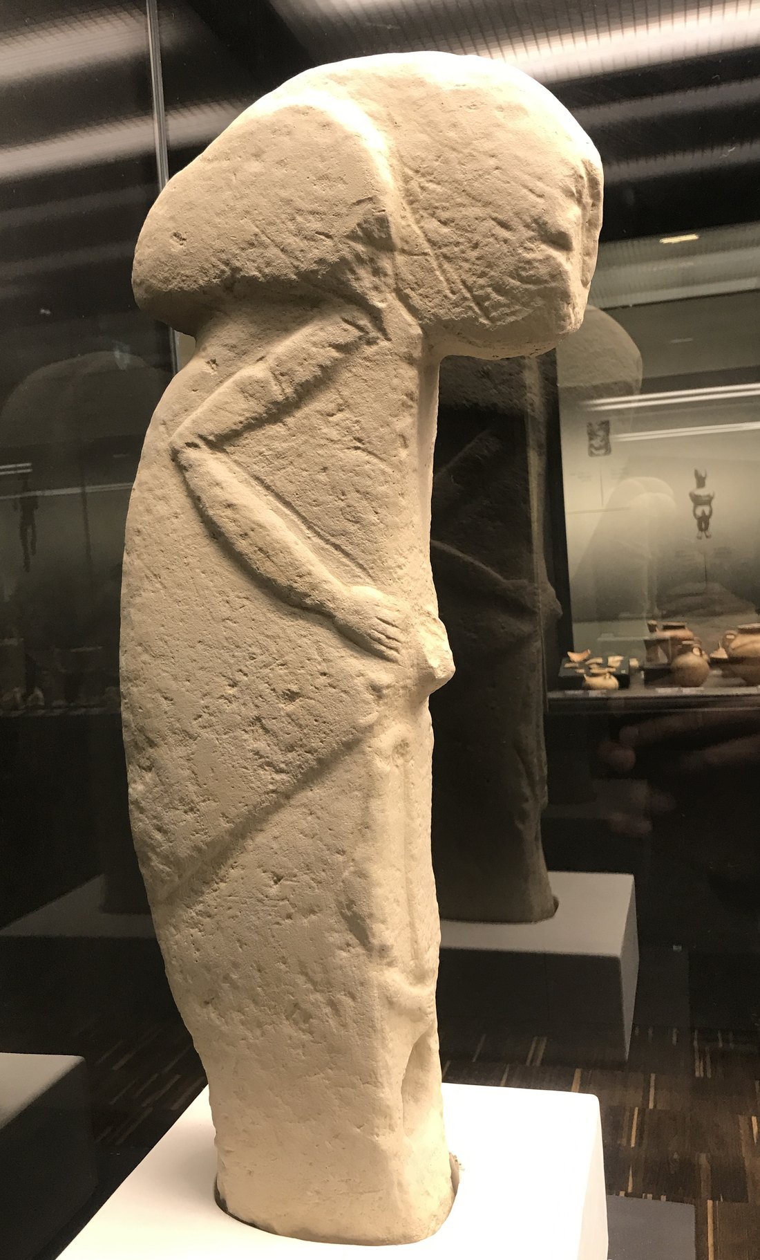 The Kilisik sculpture — a roughly 80 cm limestone figure found near Kilisik, Adıyaman, in 1965: a T-shaped head, an arm bent across the body, and hands meeting at the belly. Shown here as a museum cast. Cast: Archäologisches Museum der WWU Münster, via Wikimedia Commons (CC BY-SA 4.0).