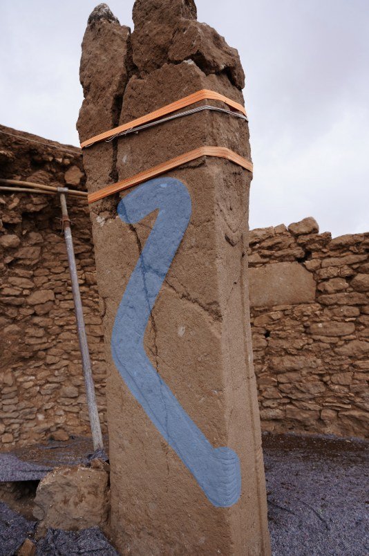 The same pillar with the arm picked out in blue: it bends sharply at the shoulder, curves down the front of the shaft, and ends in the hand with its splayed grooves. It is that shoulder — a pronounced bend rather than the clean, near-square turn of a standard T-pillar's arm — that reads as unusual, and that underlies the crane-wing reading. Highlight by researcher Dakota Wint.